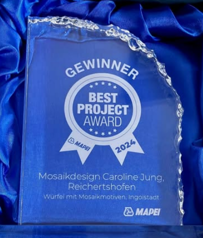 Gewinner-Trophäe "Best Project Award 2024" Glastrophäe "Best Project Award 2024" von MAPEI, verliehen an Mosaikdesign Caroline Jung, präsentiert auf blauem Seidenstoff.