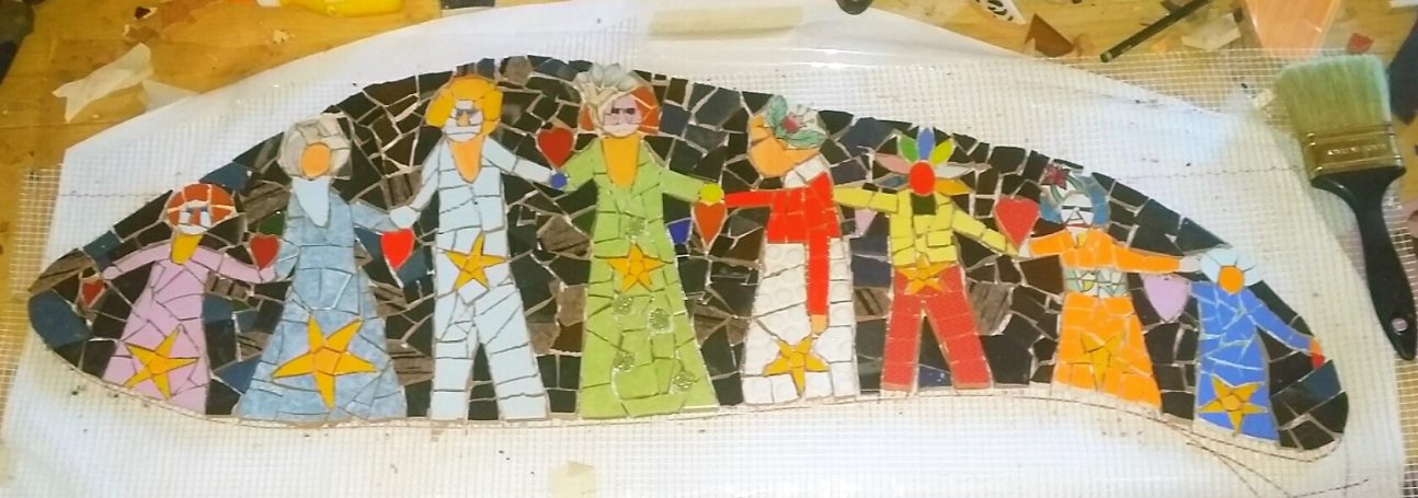 Nahaufnahme eines Mosaiks mit vier stilisierten Figuren, die sich an den Händen halten, mit Sternenmotiven auf ihrer Kleidung.