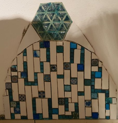 Geometrisches Wandmosaik in Bogenform mit weißen und blauen Rechtecken sowie einem sechseckigen Element.