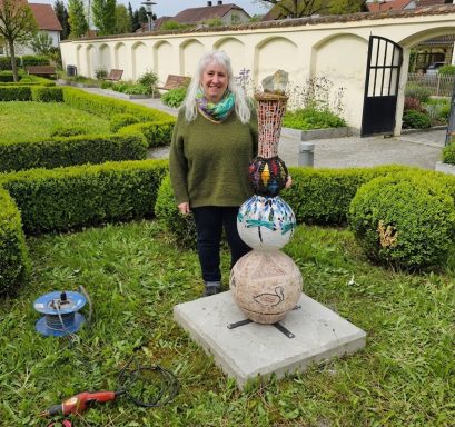 Mosaik-Totem im Barockgarten Große, mehrfarbige Mosaik-Gartenskulptur in Säulenform in einem formalen Garten mit Buchsbaumhecken.