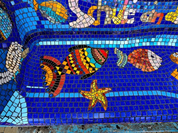 Mosaikkunst im Detail Nahaufnahme eines bunt gemusterten Fisches und eines gelben Seesterns auf leuchtend blauem Mosaik-Hintergrund.