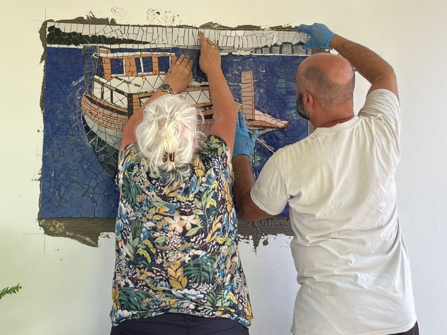 Detailansicht der Installation eines maritimen Wandmosaiks, bei der die Elemente sorgfältig in den Fliesenkleber gedrückt werden.