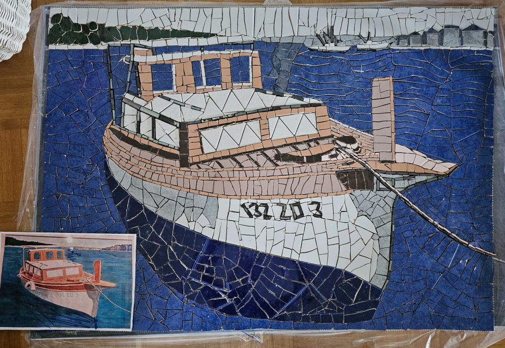 Detailaufnahme eines handgefertigten Wandmosaiks von Caroline Jung, das ein maritimes Fischerboot in blauen Farben zeigt.