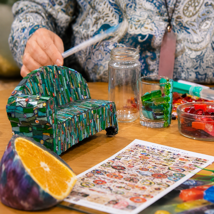 Mosaikkunst im Detail präsentiert Detailaufnahme von handgemachten Mosaik-Objekten, darunter ein grünes Miniatur-Sofa, auf dem Tisch im Fernsehstudio.