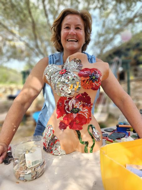 Lachende Frau hält stolz eine Mosaik-Büste mit großen roten Mohnblumen in die Kamera.