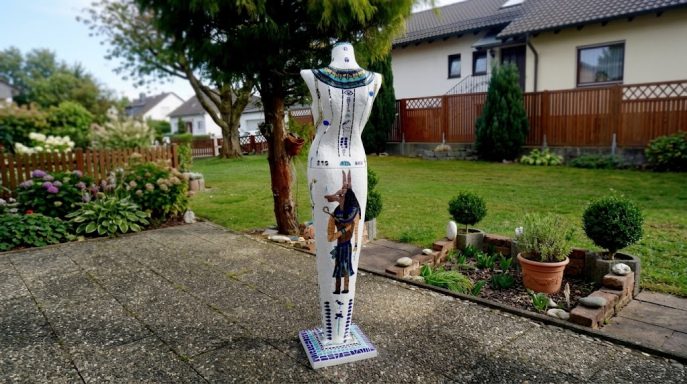 Mosaik-Torso-Skulptur Mosaik-Skulptur eines menschlichen Torsos, bedeckt mit weißen Fliesen und blauen geometrischen Mustern, stehend im Freien.
