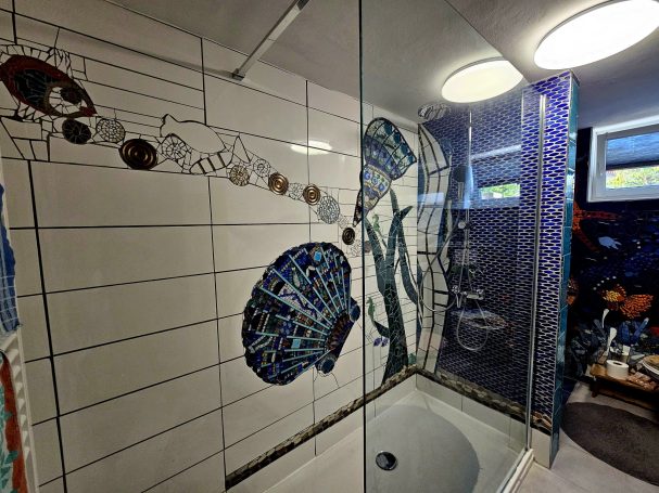 Duschbereich mit kunstvollem Muschel-Mosaik und maritimer Wandkunst von Caroline Jung.