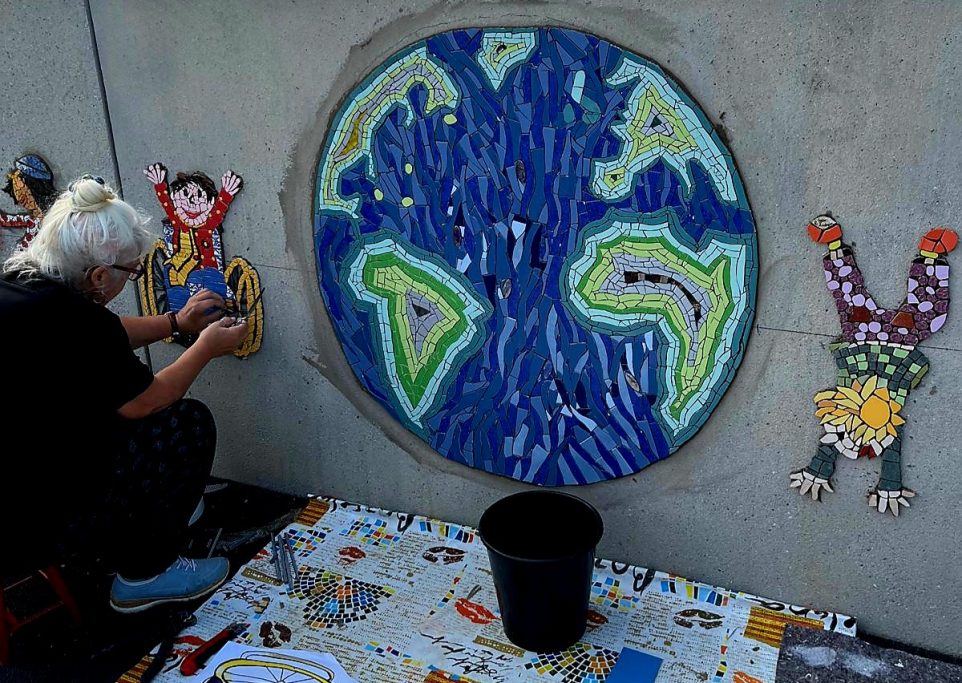 Globale Verbundenheit als Mosaik Ein großes, rundes Wandmosaik in Form einer Weltkugel mit blauen Ozeanen und grünen Kontinenten.