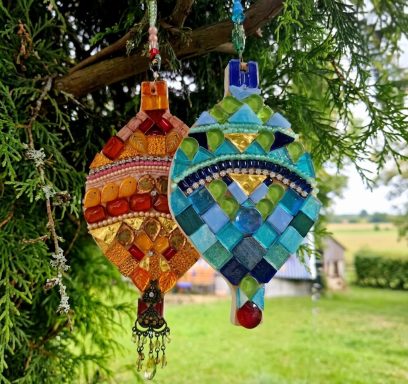 Hängende Mosaik-Kunst Bunte hängende Mosaik-Kunstobjekte, befestigt an einem Baumast im Freien.