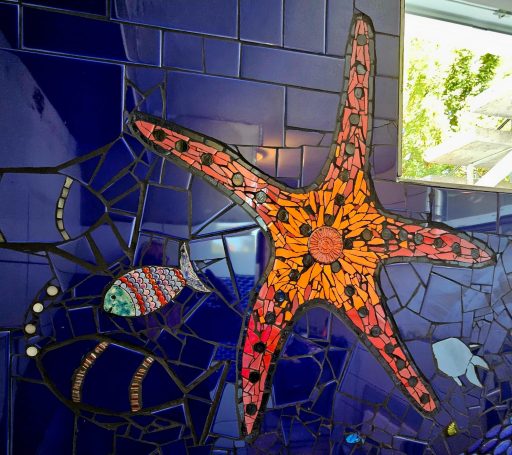 Roter Seestern als handgemachtes Mosaik auf blauen Badezimmerfliesen von Caroline Jung.