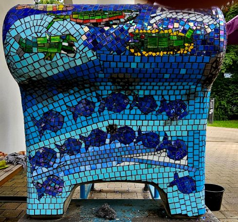 Mosaik-Sofa: Maritimes Design Rückseite eines geschwungenen Mosaik-Sofas in blauen Farben mit einer Reihe von schwimmenden Mosaik-Fischen.