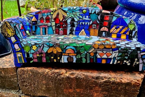 Abstraktes Mosaik-Sofa Detaillierte Ansicht eines vollständig mit bunten Mosaiksteinen besetzten Sofas im Freien.
