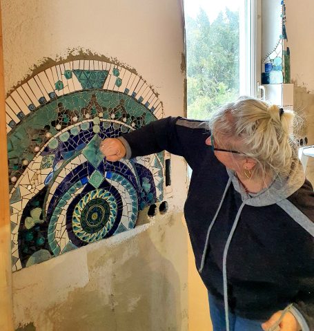 Mosaikkünstlerin Caroline Jung bei der Installation eines aufwendigen, blau-grünen Mandala-Wandmosaiks in einer Küche.