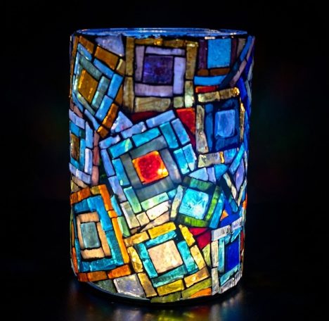 Geometrisches Mosaik-Windlicht Leuchtendes zylindrisches Mosaik-Windlicht mit geometrischen Quadratmustern in Blau, Gelb und Rot.
