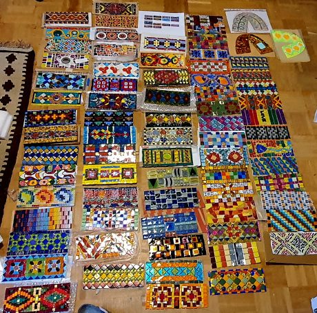 Internationale Mosaik-Beiträge Zahlreiche bunte, rechteckige Mosaikfragmente von verschiedenen internationalen Künstlern, die auf dem Boden ausgelegt sind.