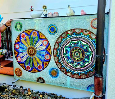 Mandala-Mosaikwand im Freien Großes rechteckiges Mosaik-Paneel im Freien mit zwei großen, bunten kreisförmigen Mandala-Mustern.