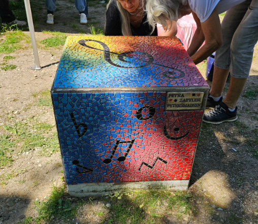 Mosaik-Würfel mit Musikmotiv Ein leuchtender Mosaik-Würfel mit schwarzen Musiknoten und einem Notenschlüssel auf einem regenbogenfarbenen Hintergrund.