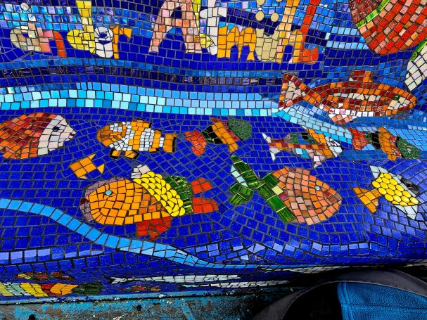 Detailansicht: Farbenfrohe Unterwasserwelt Detailaufnahme des Mosaik-Sofas mit bunten Fischen und dem Schriftzug "der Altmühl" aus Mosaiksteinen.