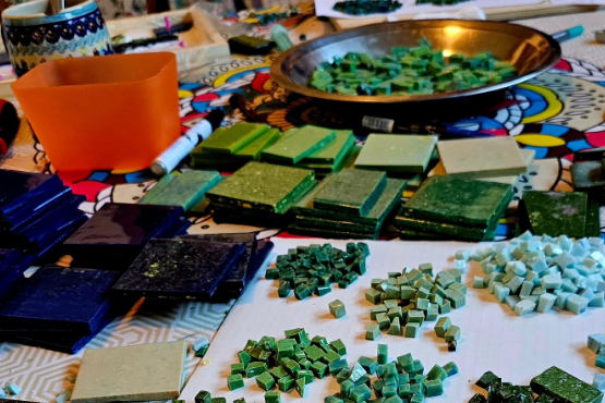 Bunte Mosaiksteine, Fliesen und Werkzeuge, die für die Materialauswahl eines neuen Mosaikprojekts auf einem Tisch vorbereitet sind.