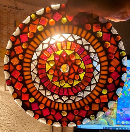 Rundes Mosaik-Licht in warmen Farben Beleuchtetes, kreisförmiges Mosaik-Mandala in warmen Rot-, Orange- und Gelbtönen, in der Hand gehalten