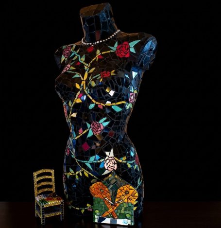 Schwarze Mosaik-Mannequin mit Rosen Schwarze Mosaik-Büste einer Frau, verziert mit rankenden rosa Rosen, vor dunklem Hintergrund.